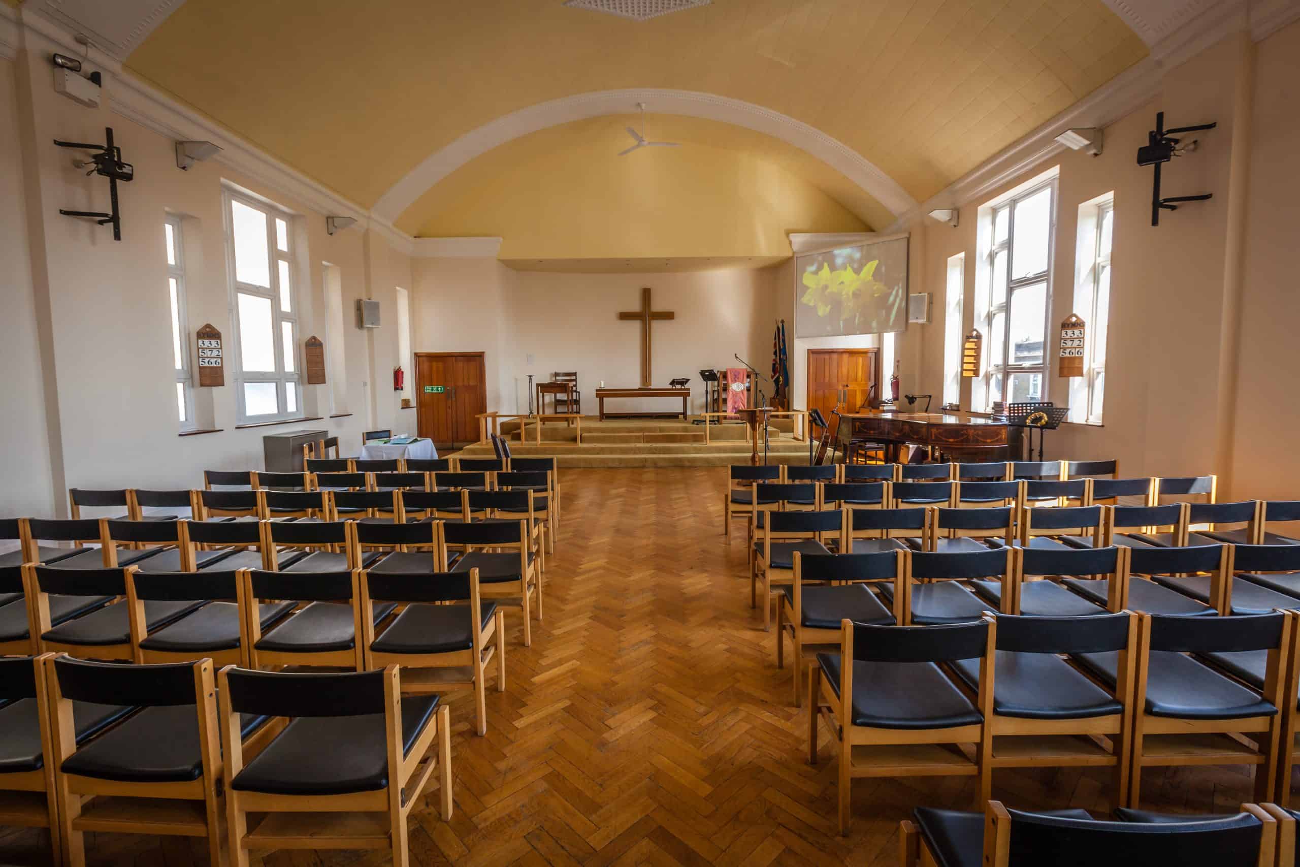 Rows of wooden pews inside a traditional church with sunlight shining through stained-glass windows, reflecting the heritage and continuity of worship.